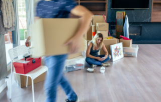 man-carrying-moving-box-while-his-wife-unpacks